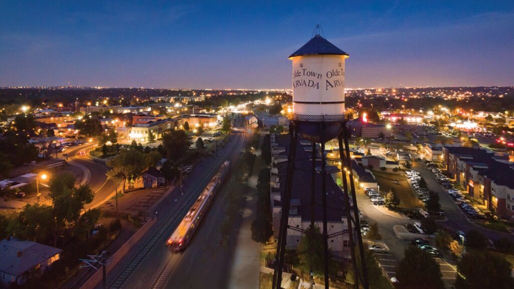 Arvada | rcastlemortgage.com Aerial view of Arvada, Colorado at night, showcasing the city skyline and a prominent water tower illuminated by city lights. Great place for homeowning. Get a quote from Robert Castle Mortgage today.
