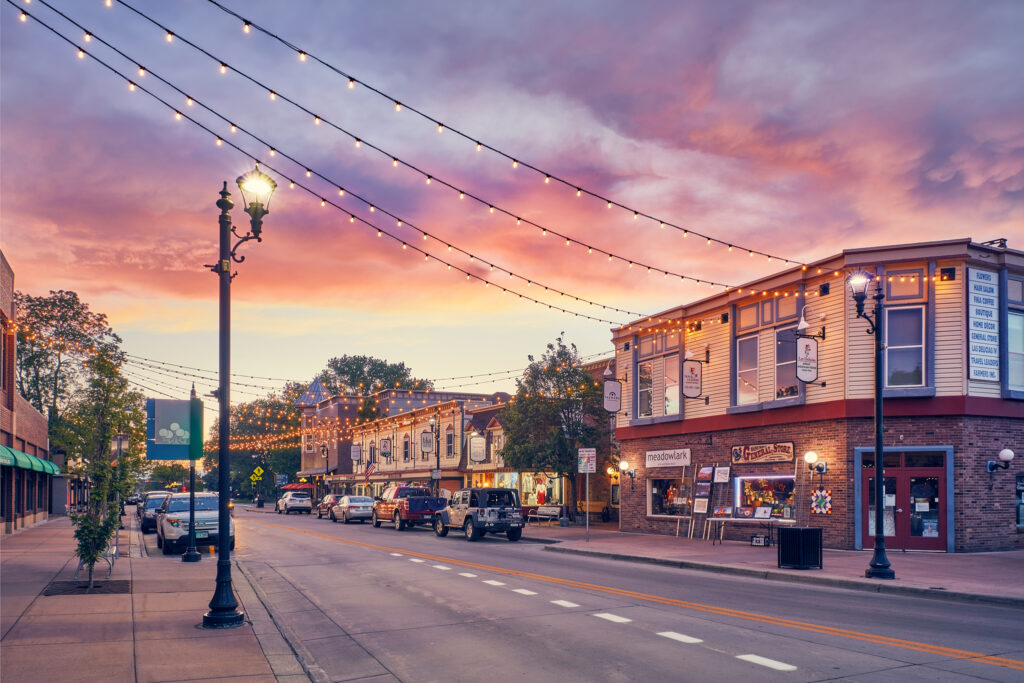 Parker | rcastlemortgage.com A city street in Parker, Colorado, featuring shops and cars, illuminated by a warm sunset glow. Great place for homeowning. Get a quote from Robert Castle Mortgage today.